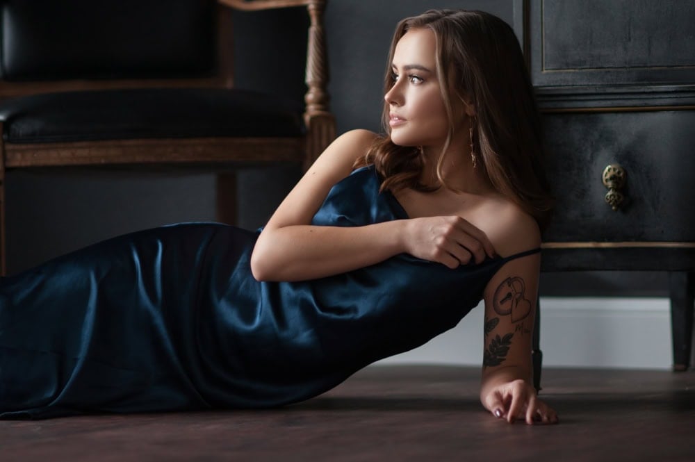 Woman in blue dress lying elegantly with tattoos visible