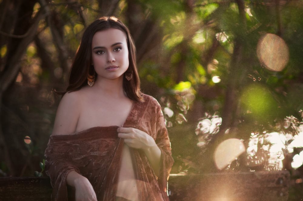 Woman in velvet dress posing in sunlit forest