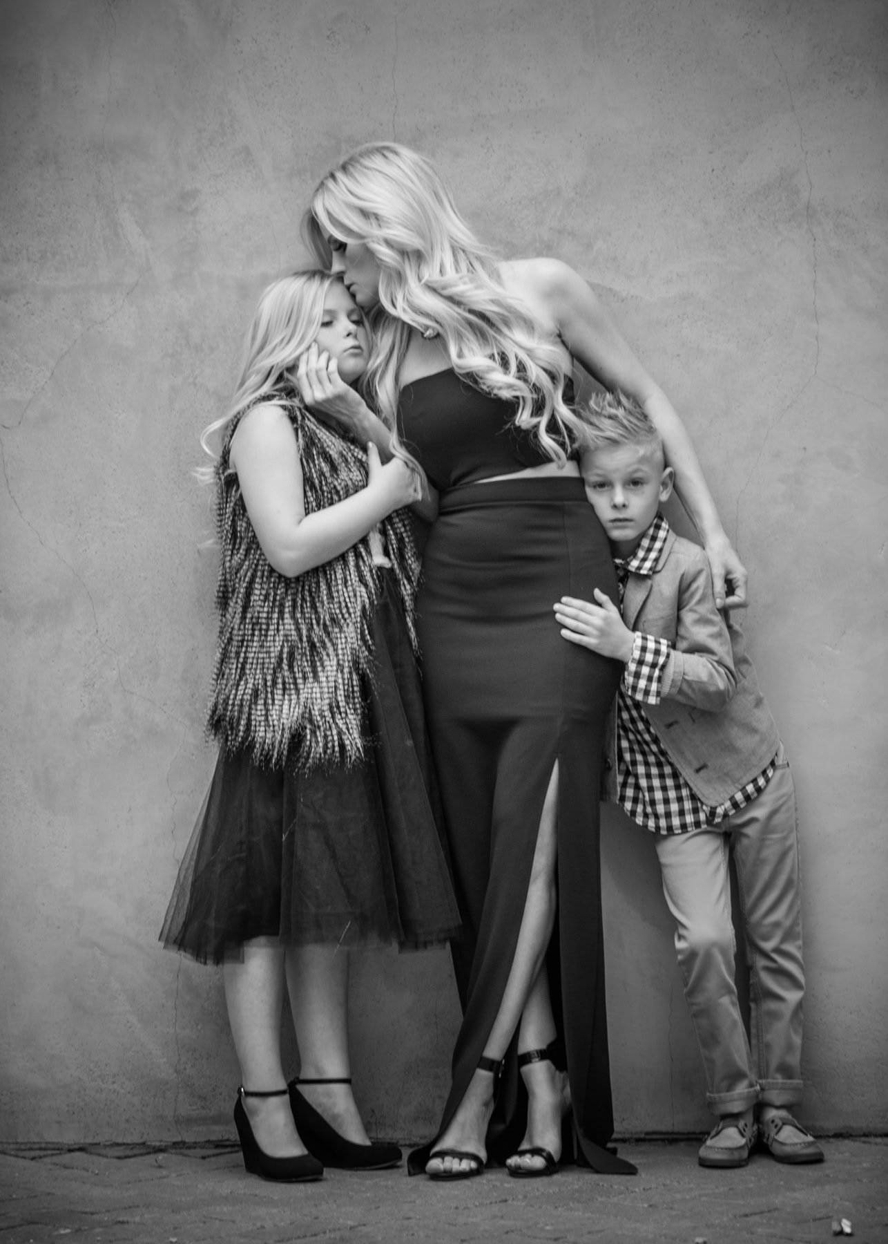 Mother embracing daughter and son against gray wall